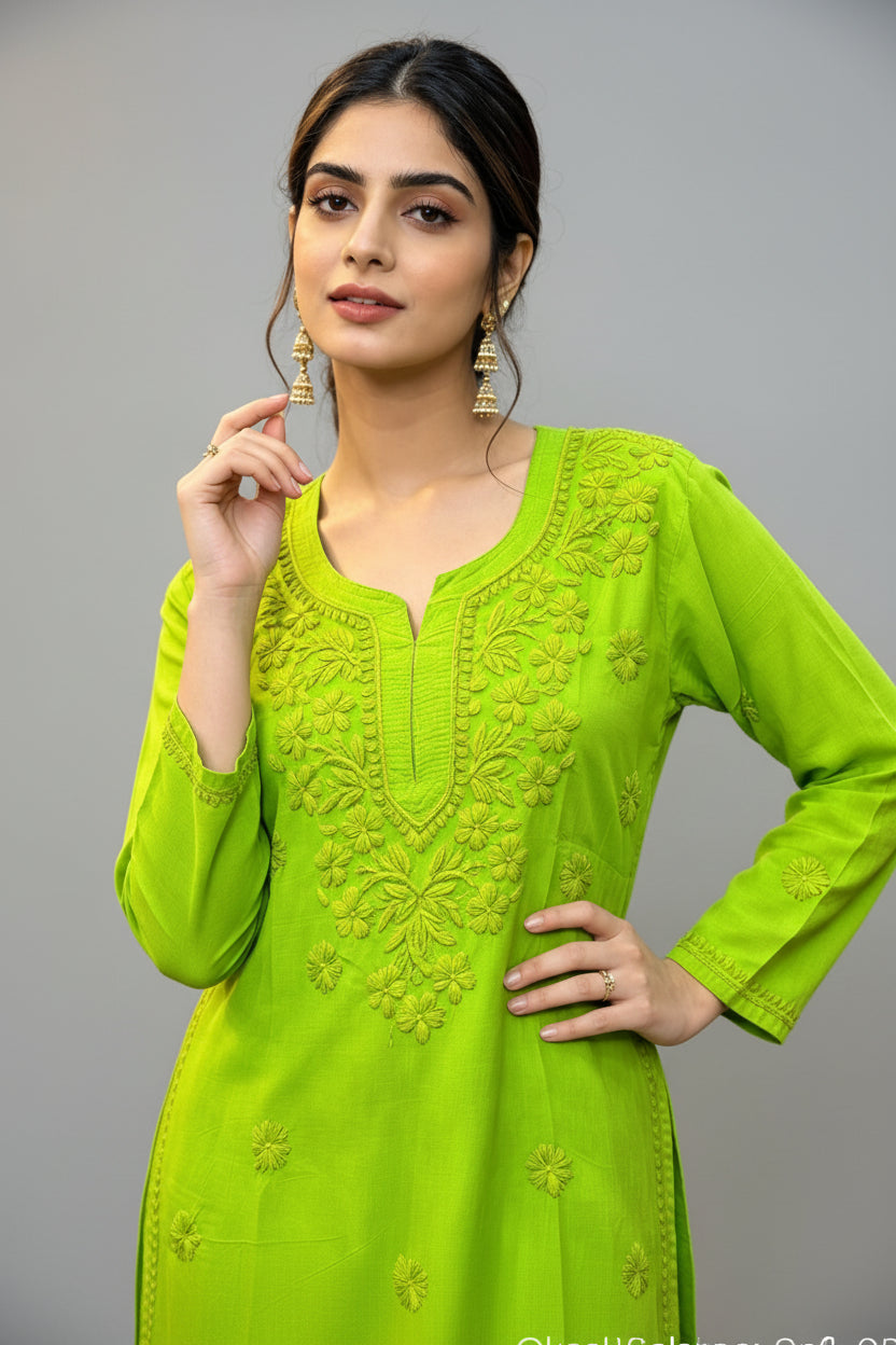 Front view of a woman wearing a vibrant lime green cotton short kurti featuring intricate matching floral embroidery, a keyhole neckline, and a square hem line, styled with traditional earrings while posing with her hand near her face.