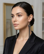 A lifestyle photograph of a model wearing long, oxidized silver statement earrings featuring an intricate mesh orb and cascading fine chain tassels, paired with a sophisticated black blazer.