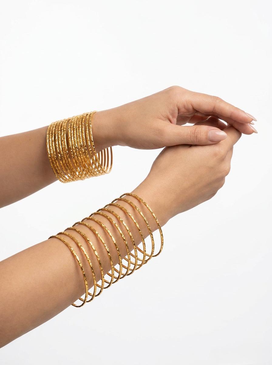 A clean lifestyle photograph demonstrating a versatile styling of 12 micro gold-plated copper bangles with an intricate diamond-cut texture, worn elegantly across both wrists against a bright white background.