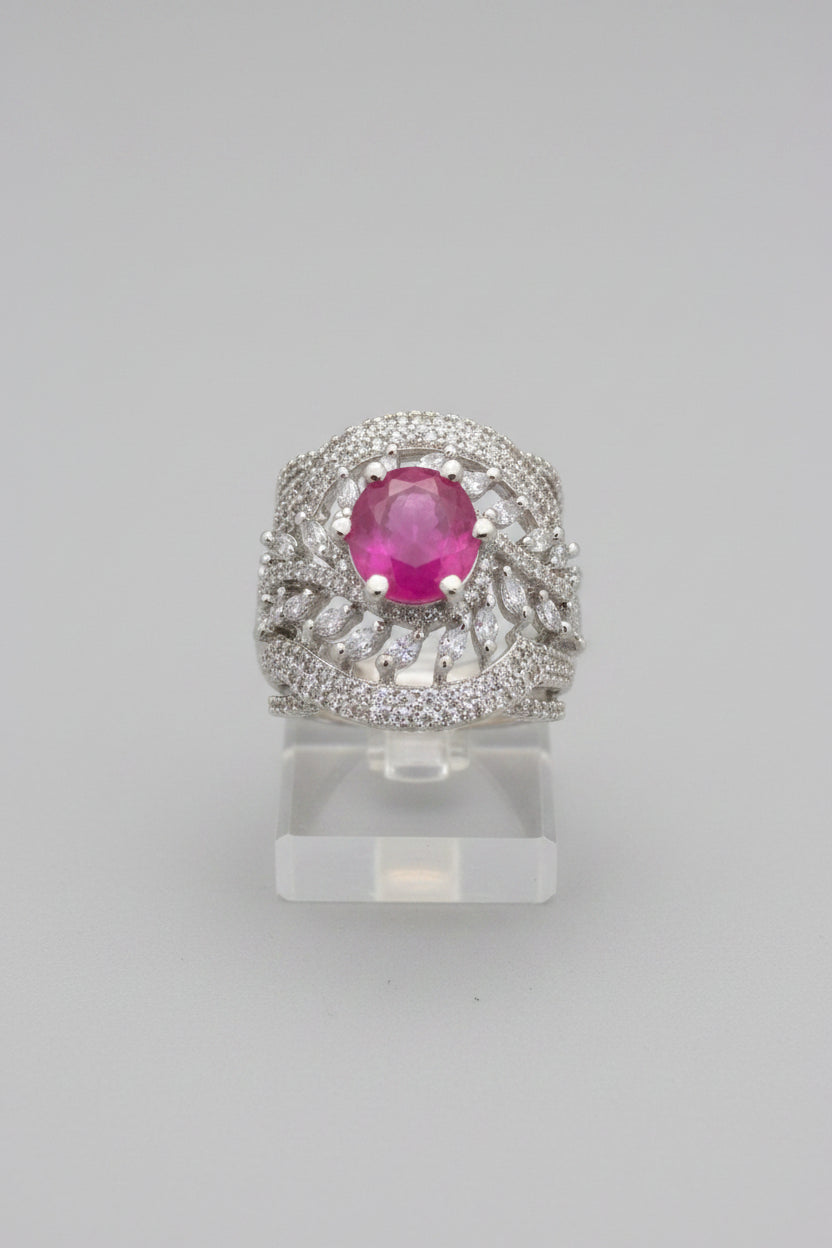 Luxurious silver-tone cocktail ring featuring a round vibrant ruby pink centre stone surrounded by marquise and round-cut cubic zirconia accents in an intricate halo setting, with a textured honeycomb-patterned band, displayed on champagne and emerald green satin, premium American Diamond jewellery.