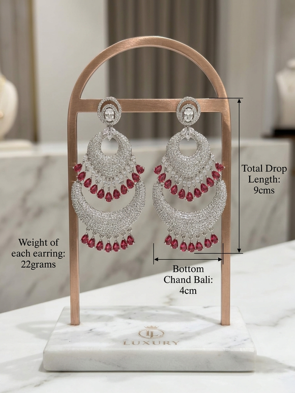 Luxury American Diamond and ruby gemstone chaand bali statement earrings in a silver finish. Features tiered crescent layers with dangling teardrop red stones, perfect for bridal and festive wear