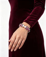 Luxury silver cuff bangle with deep purple stones and white pearls worn on wrist — Famaza Couture elegant statement jewelry, silver-tone open cuff design with sparkling crystals and lustrous pearls, bridal and party wear bracelet displayed on model in burgundy velvet dress against clean white background.