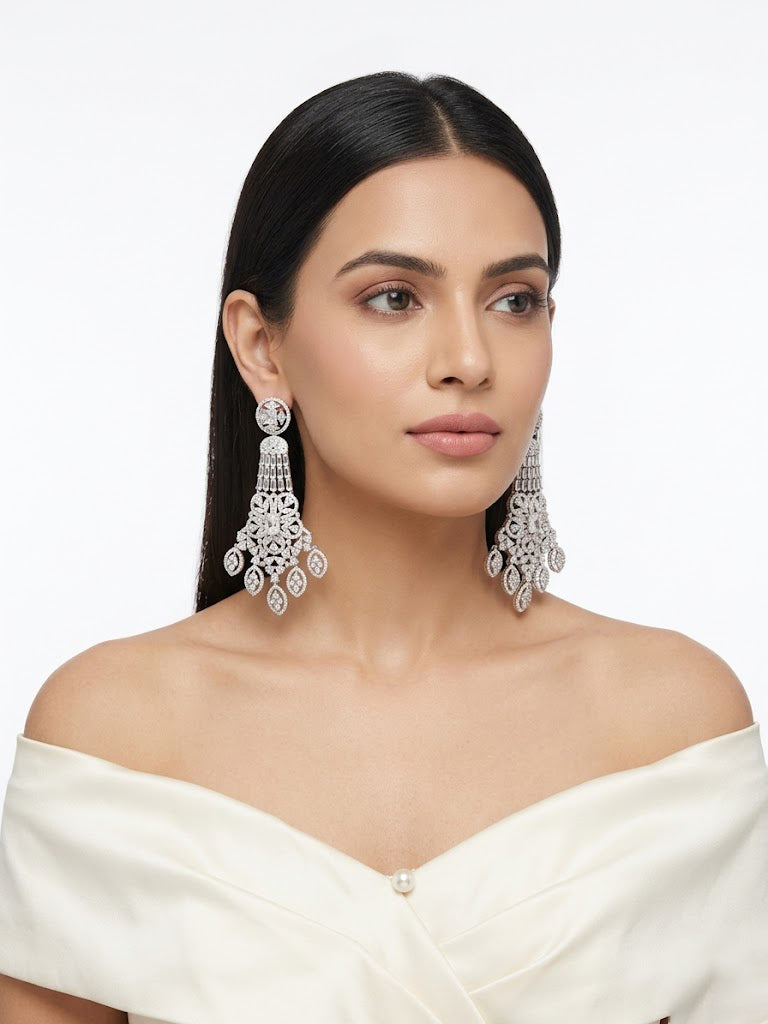 Luxury long American Diamond chandelier earrings in a classic silver finish. Tiered geometric cascade design encrusted with shimmering white crystals, styled on a model for bridal or evening wear.