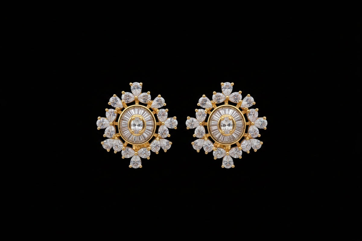 Gold-toned statement earrings with clear round and marquise-cut stones, shown worn on a hand against a dark textured background.
