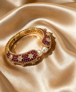 Magenta Pearl Gold Openable Bangle resting on champagne gold satin — luxury bridal jewelry featuring deep magenta-ruby gemstones, lustrous pearls, and intricate gold craftsmanship; premium bridal accessory by Famaza Couture