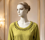 Mannequin wearing a green top with intricate detailing in a softly lit room.