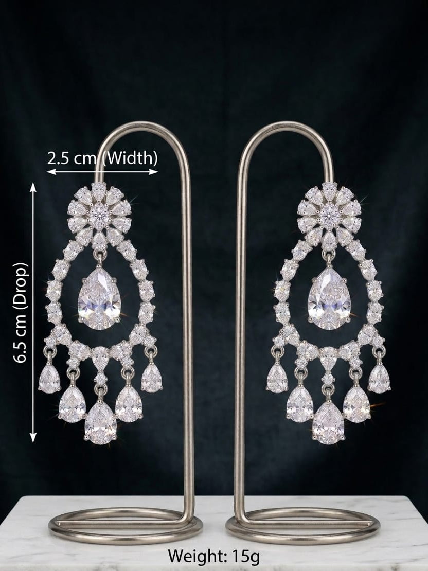A pair of silver-tone drop chandelier earrings with clear teardrop and floral crystals, displayed on a white marble block against a black background. White text overlays show dimensions (2.