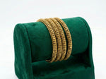 A professional product photograph of four micro gold-plated copper bangles displayed on a green velvet jewelry roll. The bangles feature an intricate, repetitive honeycomb-style textured pattern with a high-shine finish, set against a clean white background.