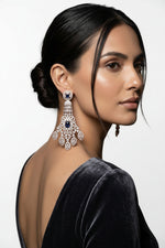 A detailed view of a luxurious, multi-tiered white gold chandelier earring featuring intricate diamond clusters and two prominent blue sapphires, set against a dark, elegant background on a model.
