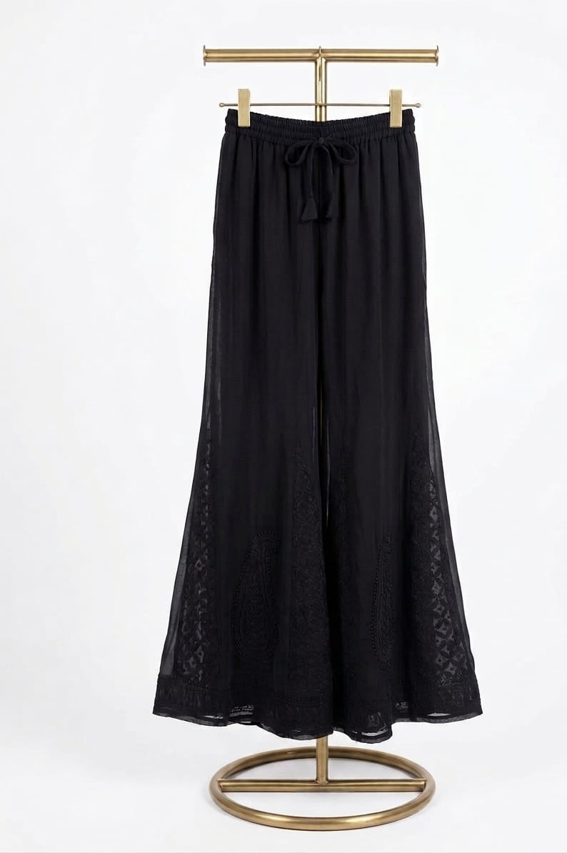 A pair of black georgette palazzo pants featuring intricate Bakhiya embroidery, displayed on a gold post stand against a pure white background.
