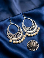 Silver-toned crescent-shaped filigree earrings with dangling cream pearl beads, displayed on a dark blue satin fabric alongside a matching round earring back.