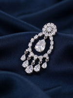 A silver-toned chandelier-style brooch with clear teardrop and round gemstones, displayed on dark navy blue draped fabric.