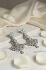 Statement 7.5cm silver earrings with mint green accents and clear crystal embellishments on a marble display stand.