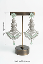 Pair of silver earrings with green accents on a stand, showing dimensions and weight.