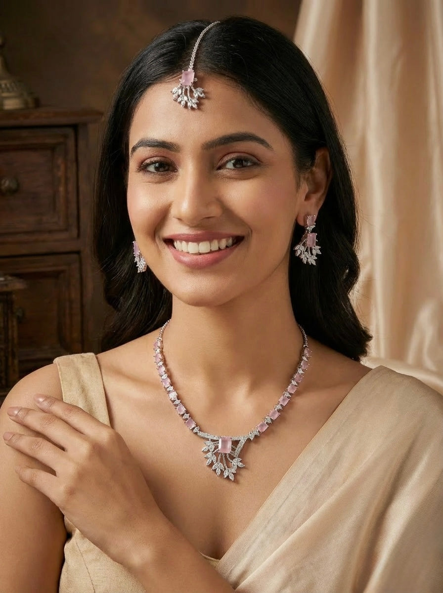 Model is wearing American diamond jewellery set including necklace, earrings and maang tikka with pink centre stone. 