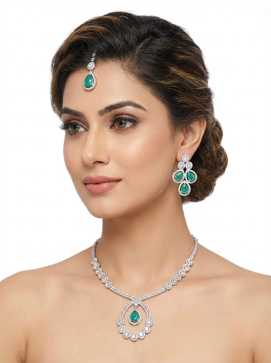 Model is wearingThe American diamonds bridal jewellery set including necklace, earrings and maang tikka with sea green colour central cubic zirconia stones. 