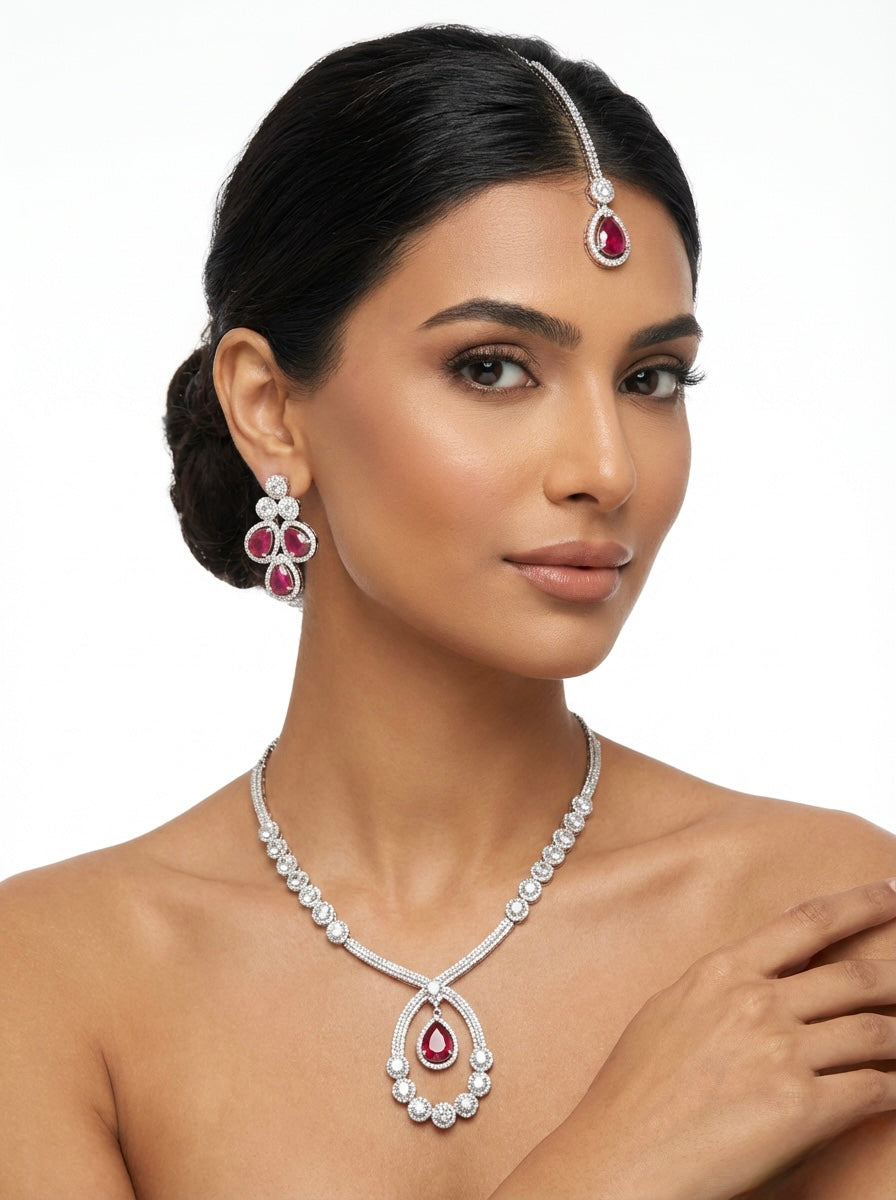 Model is wearingThe American diamonds bridal jewellery set including necklace, earrings and maang tikka with ruby colour central cubic zirconia stones. 
