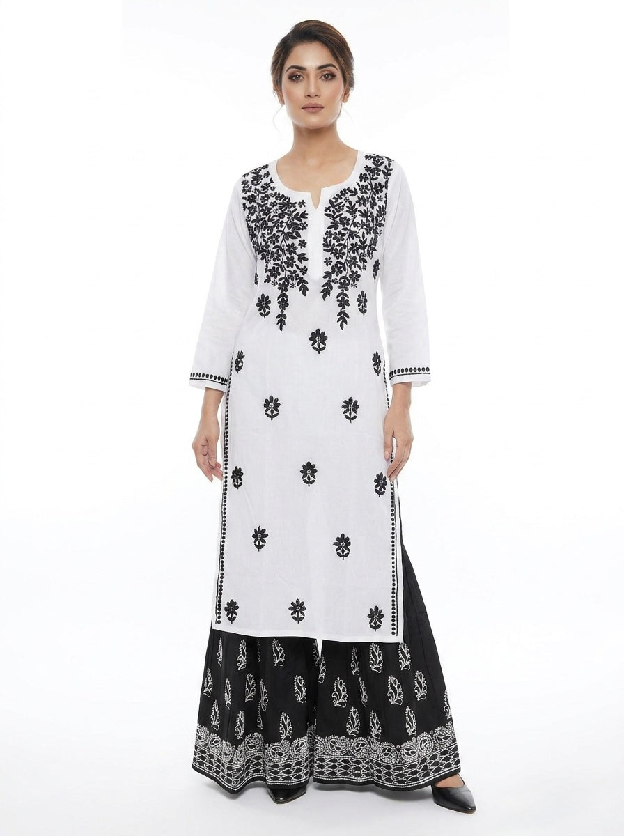Model is wearing a white outfit with black floral hand embroidery on a white background with black trousers . 