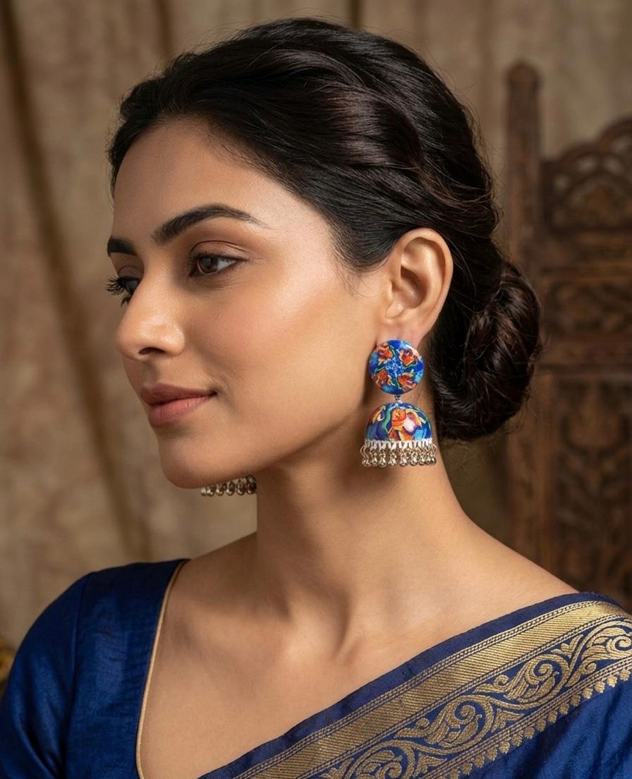 Model wearing hand-painted enamel jhumka earrings with blue Koi fish design and dangling metallic beads.