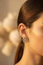 Model wearing the golden wheel-shaped stud earrings intricately detailed with sparkling clear CZ stones.