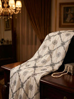 An elegant white and black floral lattice embroidered dupatta draped over a dark wooden table next to a pearl necklace and vintage trinket box, showcasing a luxurious and classic aesthetic.