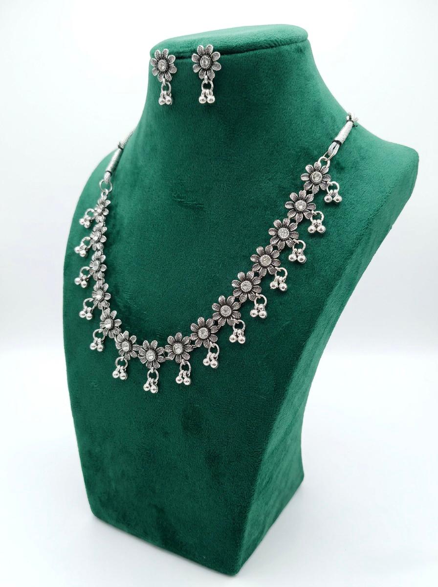Front view of an antique oxidized silver sunflower-motif jewelry set with clear crystal centers and triple-bead ghungroo drops displayed on a green velvet mannequin stand.