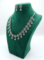 Front view of an antique oxidized silver sunflower-motif jewelry set with clear crystal centers and triple-bead ghungroo drops displayed on a green velvet mannequin stand.