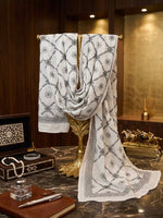 A monochrome white Kota Doriya dupatta with black floral lattice embroidery, elegantly draped over a gold decorative stand in a luxury room setting, accompanied by a pearl necklace and vintage accessories.