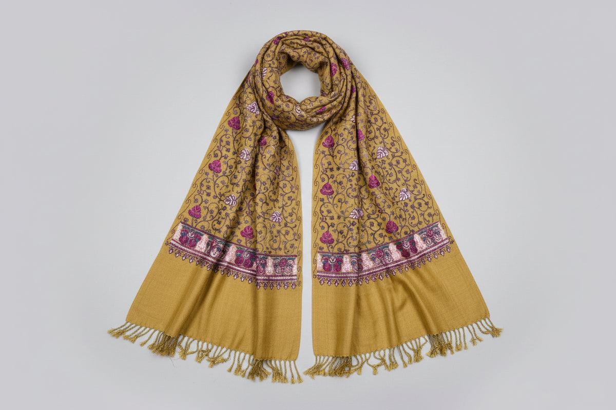 Mustard base colour Kashmiri embroidered pashmina scarf with maple leaf motifs and tassels on the ends, displayed on a wooden surface.