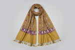 Mustard base colour Kashmiri embroidered pashmina scarf with maple leaf motifs and tassels on the ends, displayed on a wooden surface.