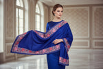 Navy blue shawl with floral patterns draped over a mannequin next to a black handbag on a small table against a marble wall.