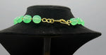 Necklace closure with apple green beads on a black mannequin bust against a grey background