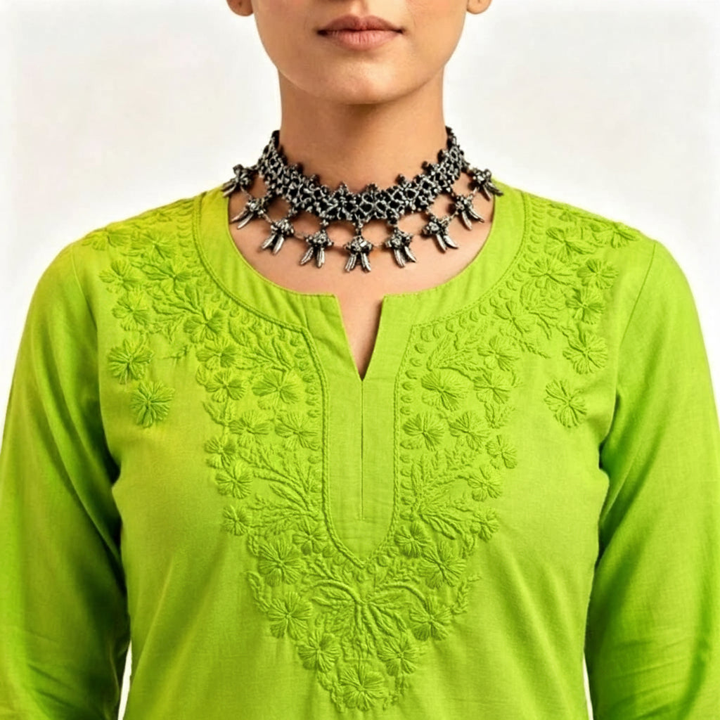 Close-up view of the neckline and chest area of a vibrant lime green cotton short kurti featuring dense, intricate floral embroidery and a keyhole neckline, styled with an ornate silver choker necklace.