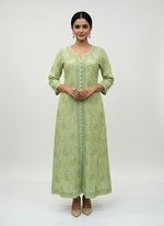 Olive green dress with floral patterns on a grey surface with small decorative items.