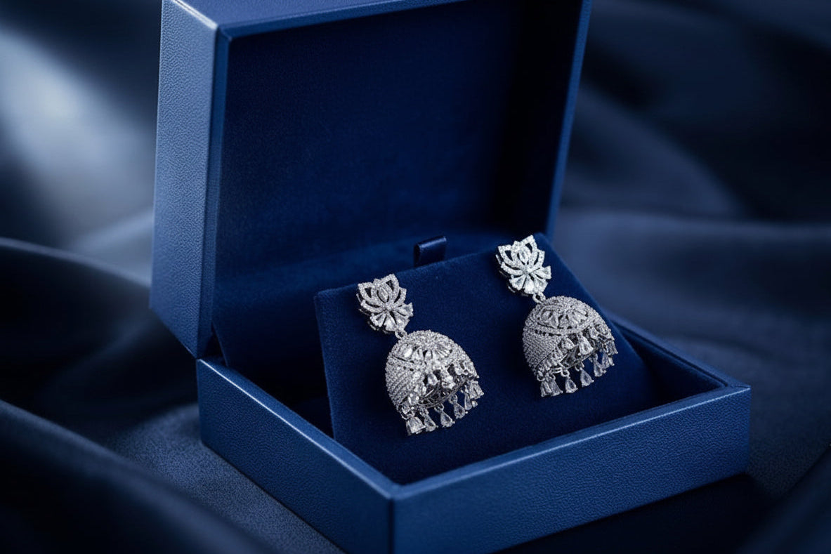 A pair of silver-toned elephant-shaped dangle earrings displayed in an open navy blue Aria Imperial jewelry box on a dark blue fabric background.