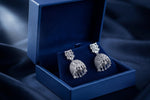 A pair of silver-toned elephant-shaped dangle earrings displayed in an open navy blue Aria Imperial jewelry box on a dark blue fabric background.