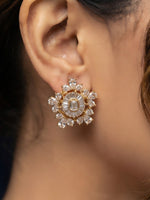 A close-up of a model's ear wearing a gold-toned, multi-stone cluster earring with clear crystals.