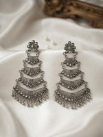 A pair of ornate silver-toned tiered chandelier earrings with dangling bead details, displayed on draped white satin fabric.