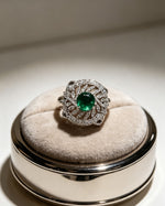 Luxurious silver-plated halo cocktail ring with a round vibrant emerald green center stone, surrounded by marquise and round-cut cubic zirconia accents in an intricate filigree design, displayed on a premium velvet ring stand, elegant women's AD jewelry.