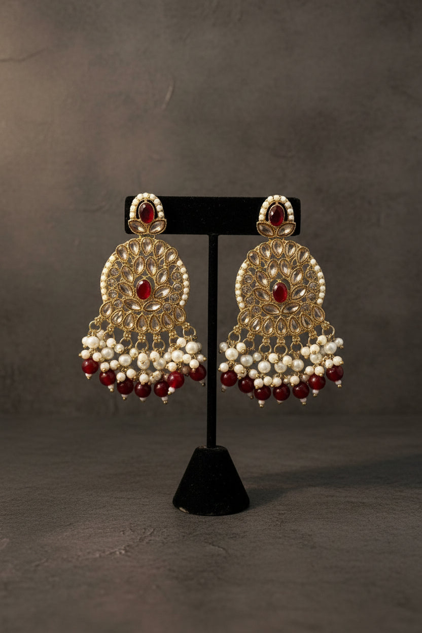 Ornate earrings with pearls and red stones on a black stand. 