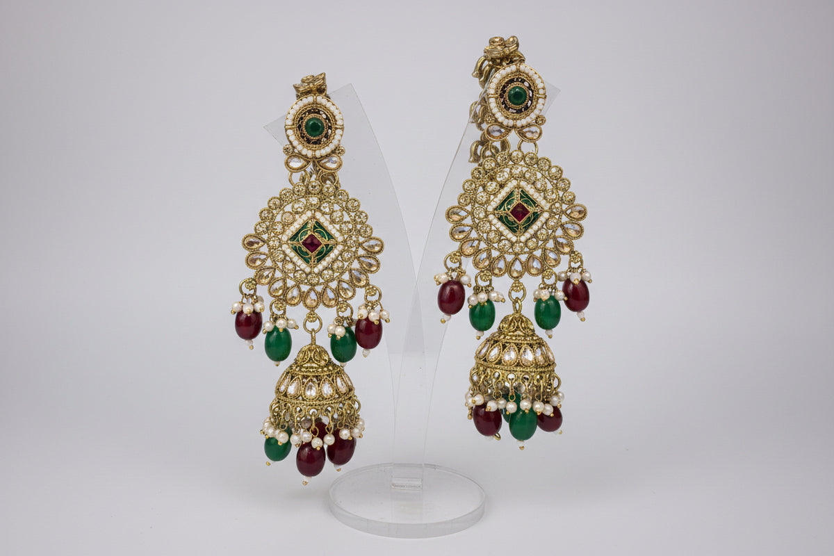 Ornate gold earrings with green and red stones on a black background