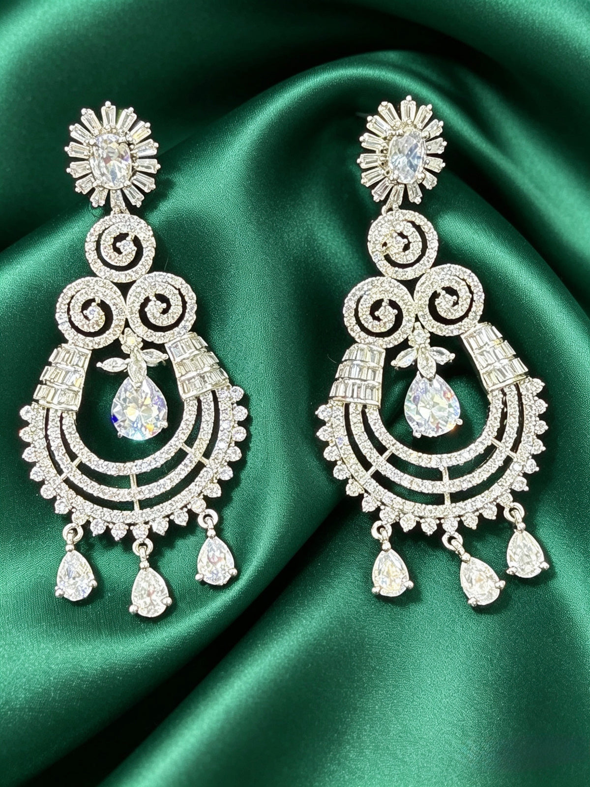 Ornate silver earrings with clear stones on a green satin background
