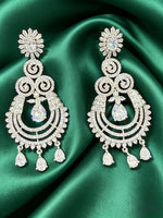 Ornate silver earrings with clear stones on a green satin background