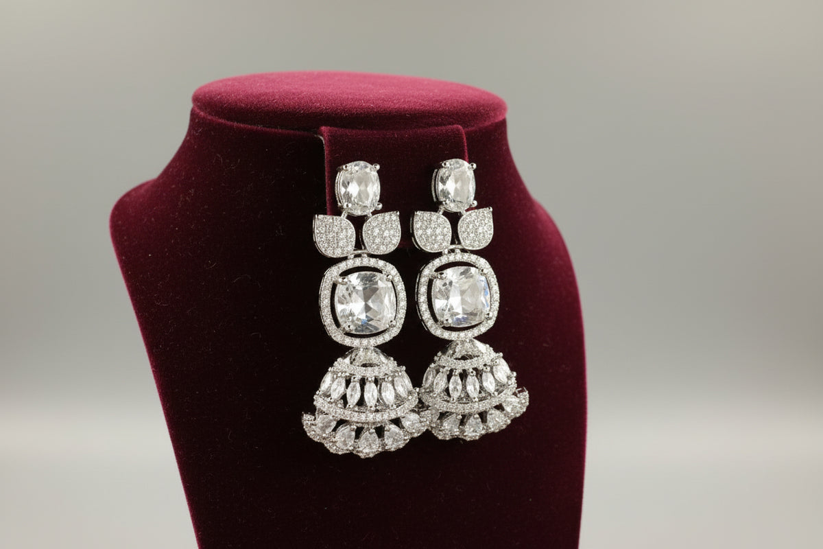 Ornate silver earrings with gemstones on a black stand