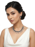 Model wearing an oxidized silver-toned floral choker necklace featuring ruby and emerald nano stones and matching floral drop earrings with ghungroo beads.