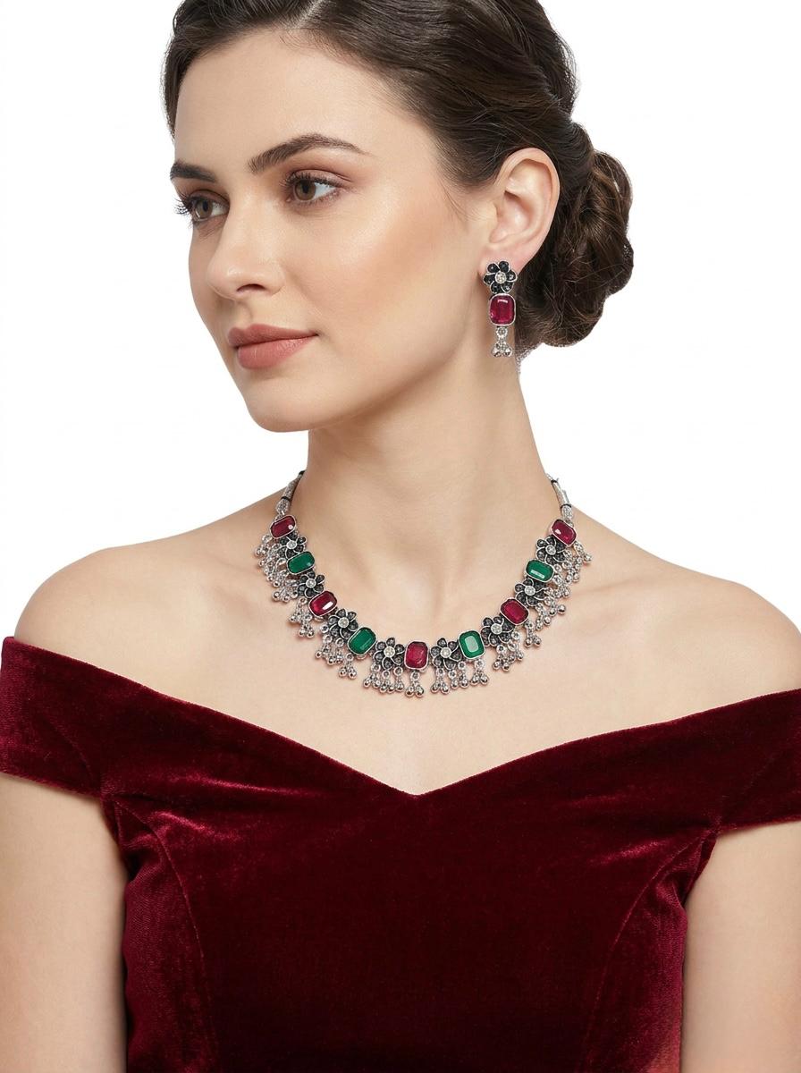 Model wearing the oxidized floral necklace and matching earrings featuring pink and green stone accents and a traditional silver lattice design.
