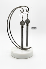 Black tassel earrings on a stand with measurement label