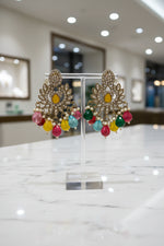 Pair of brass earrings with colorful beads on a black stand against a textured white background