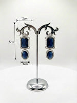 Pair of earrings with blue stones on a stand with measurements