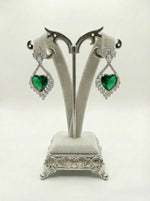 Pair of earrings with green heart-shaped stones on a decorative stand against a white background